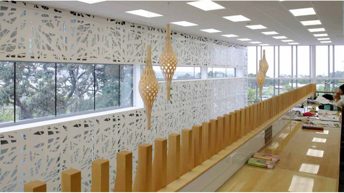 REAR WALL INTERIOR: The strip window in the rear wall of the building was positioned to capture wide views to Auckland harbour, as well as to mature Pohutukawa trees, from the mezzanine floor. On the wall, patterned boards laser-cut and painted white cover concrete tilt slabs and some vertical windows. These screens are removable. Alaskan Yellow Cedar was used on the balusters.
